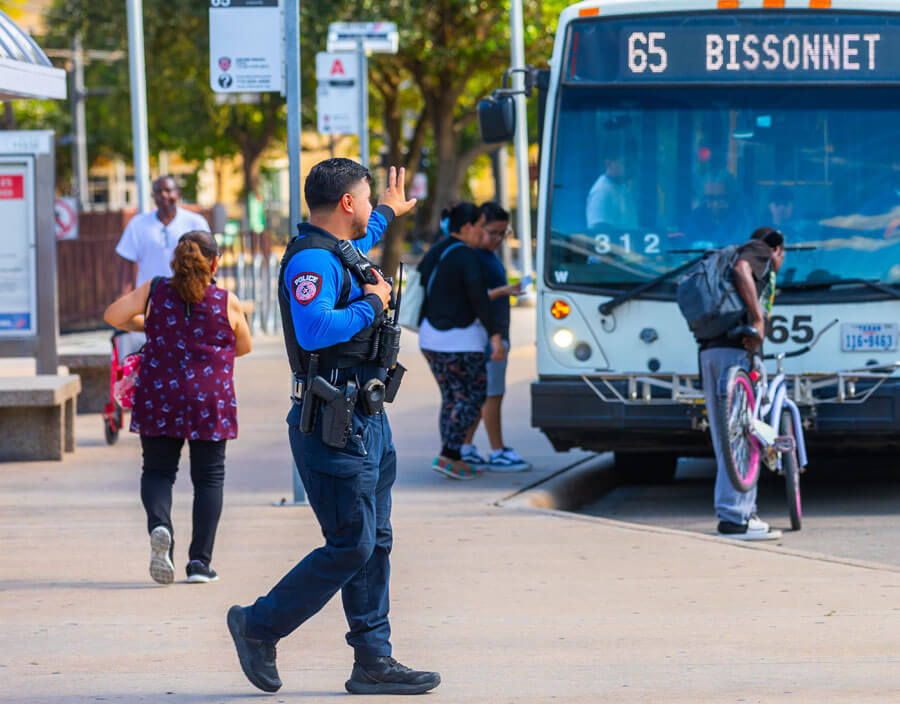 METRO Police officer waving his hand toward bus operator as customers are boarding the 65 Bissonnet local bus, while one rider is loading a bike on the bike rack.